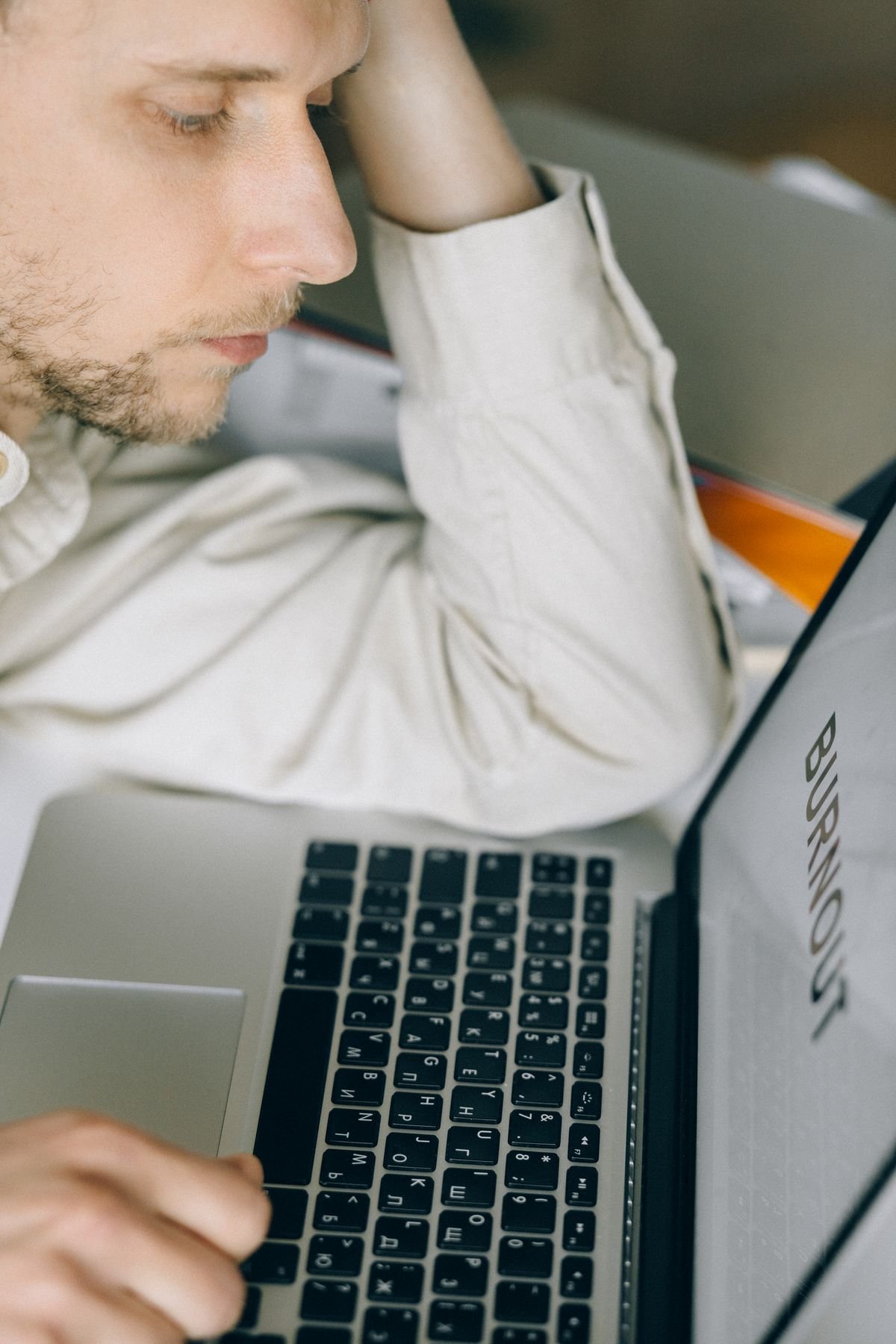 Pessoa com a cabeça apoiada na mão em frente a notebook com a palavra Burnout na tela