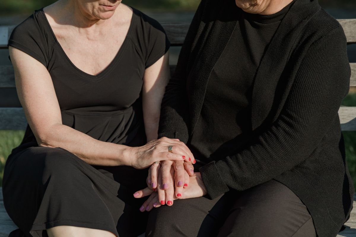 Duas mulheres de luto sentadas em um banco, de mãos dadas