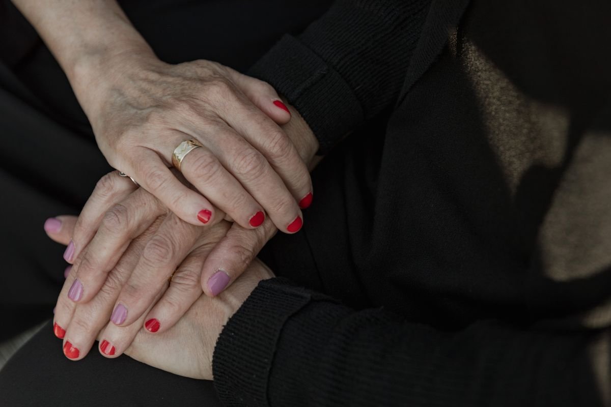 Mãos entrelaçadas em gesto de conforto, roupas escuras
