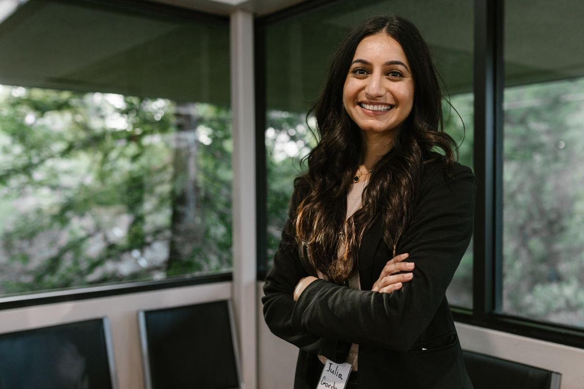 Mulher sorridente com crachá de identificação, braços cruzados, em ambiente corporativo