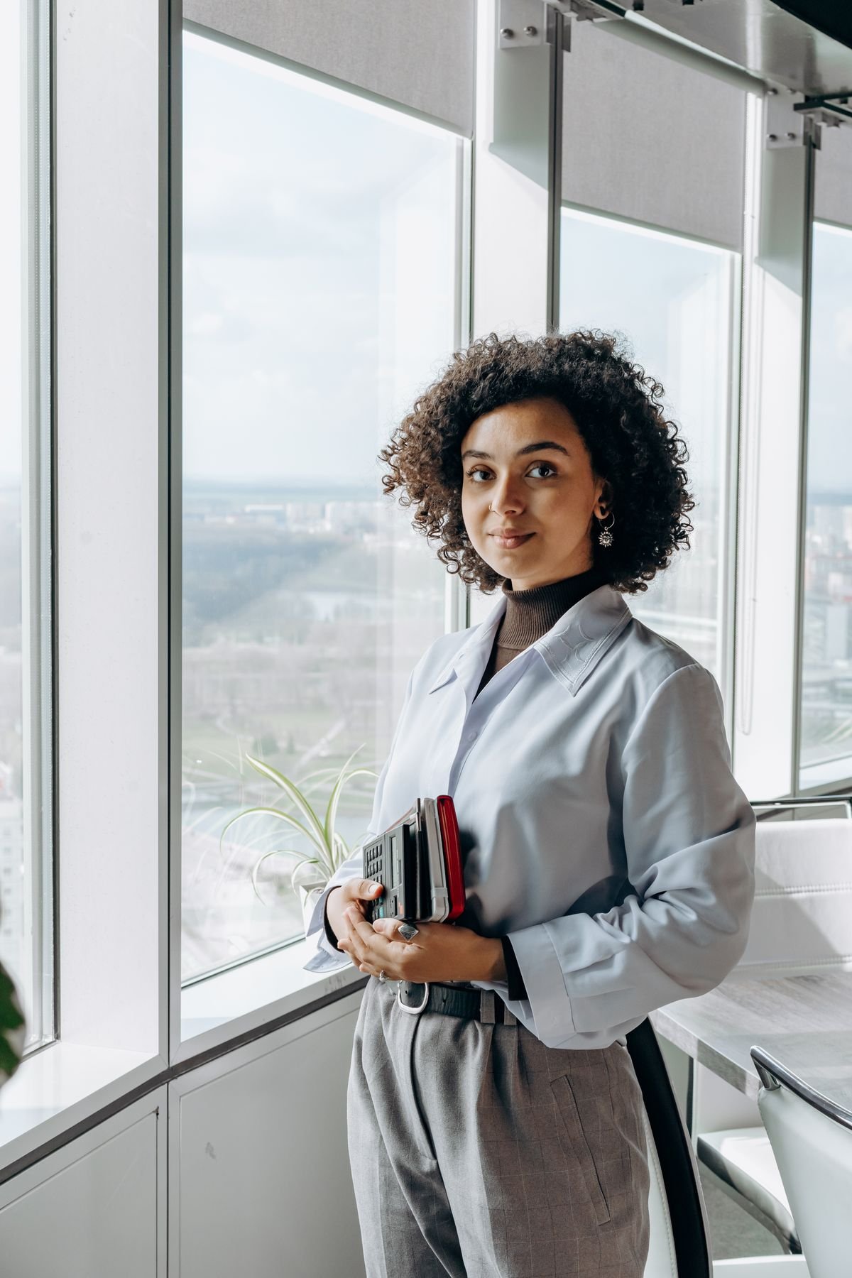 Mulher em ambiente corporativo segurando itens de trabalho, olhando para a câmera