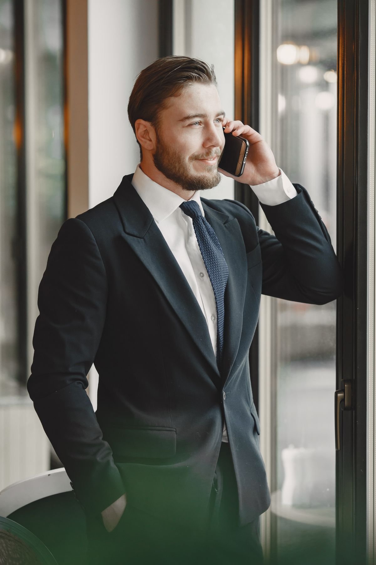 Profissional de terno ao telefone, sorridente, em escritório com vista para a cidade