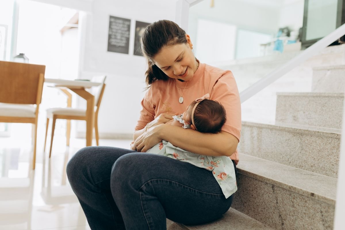 Mãe sorridente segurando o bebê no colo, sentada em uma escada